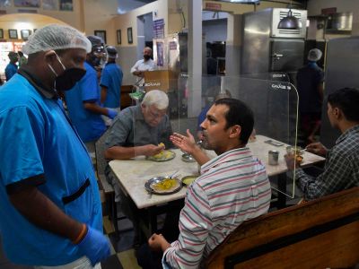 A customer talks to a waiter in a mask while eating his meal at a table divided with transparent panels in Bangalore, India.